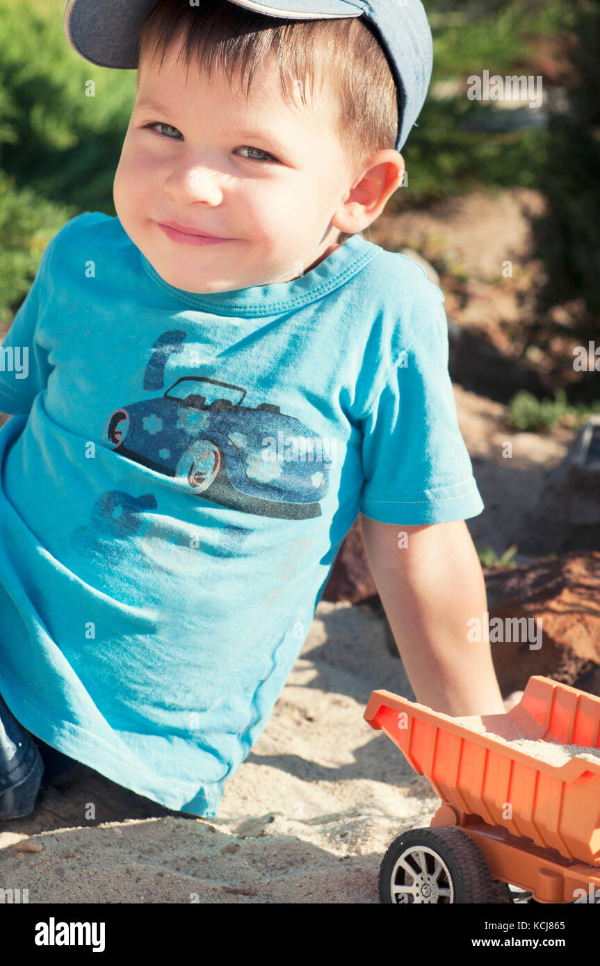 A child plays in the sand with big toy cars, an excavator, a truck Stock Photo