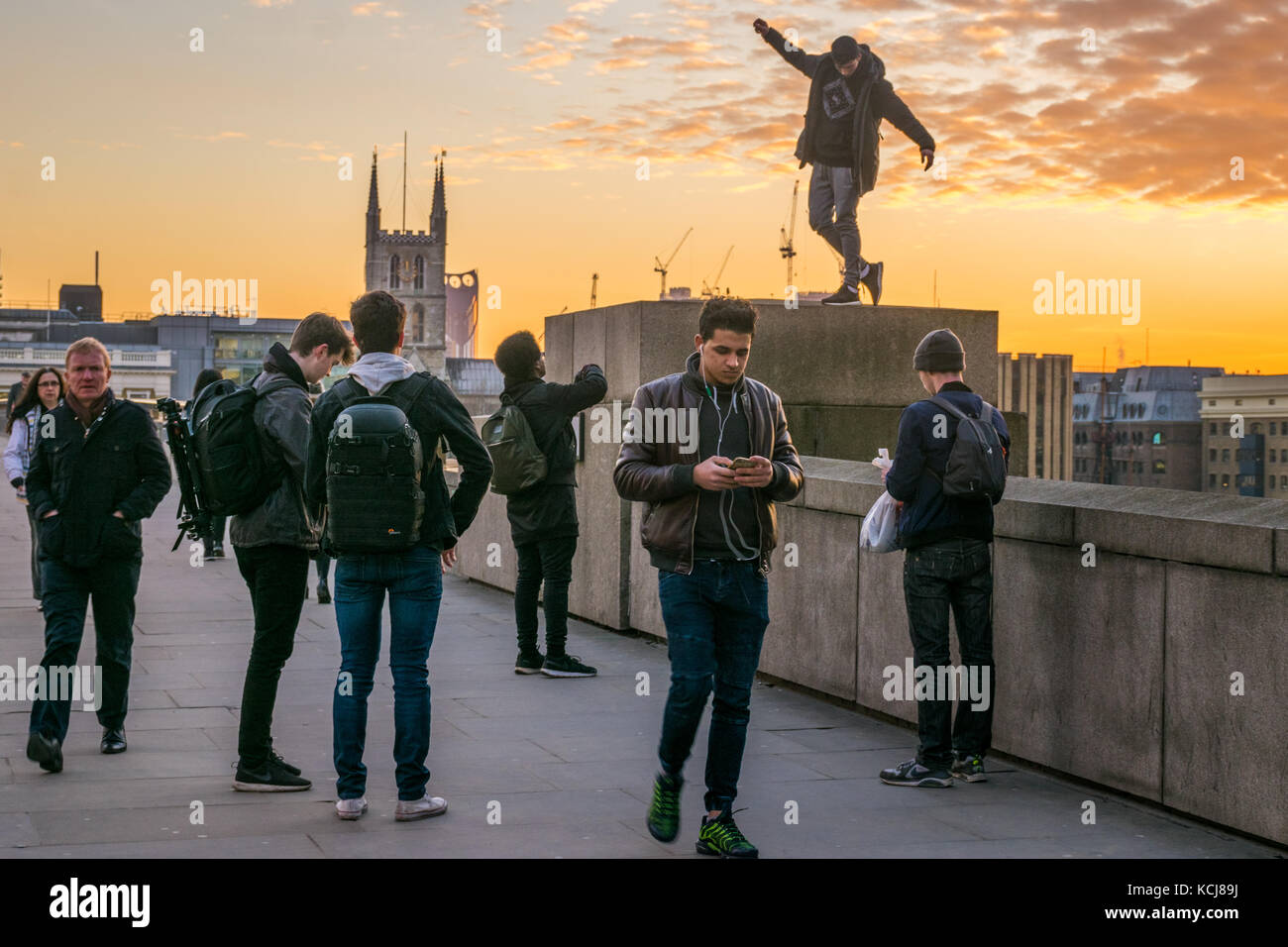Male youths taking selfies on London Waterloo Bridge at sunset Stock Photo