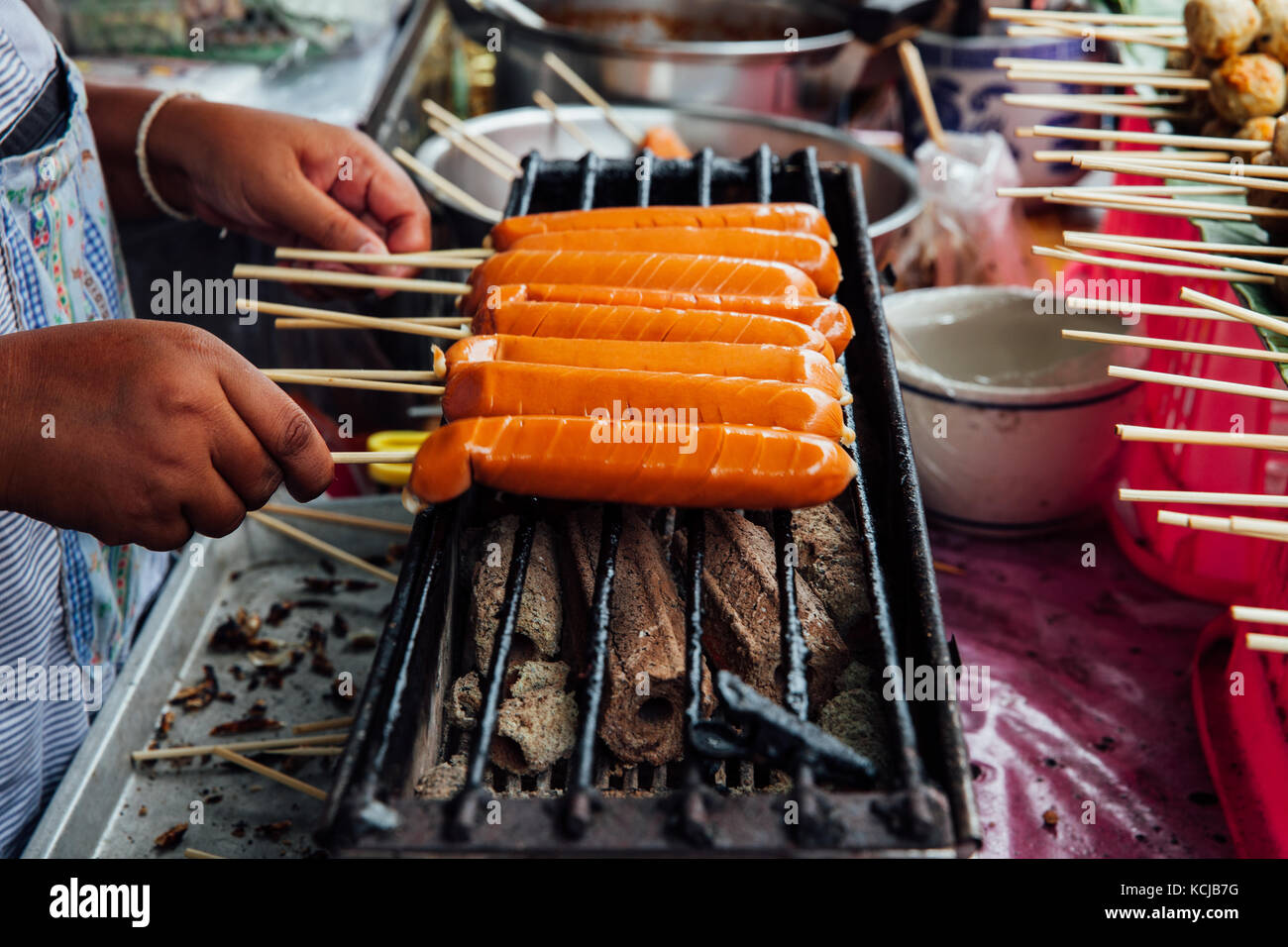 A street vendor makes grilled Thai sausages on skewers at the Warorot Market, Chiang Mai, Thailand. Stock Photo