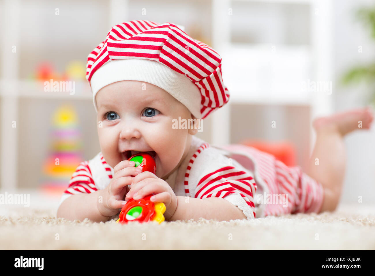 Child girl biting a toy lying on a carpet at home Stock Photo