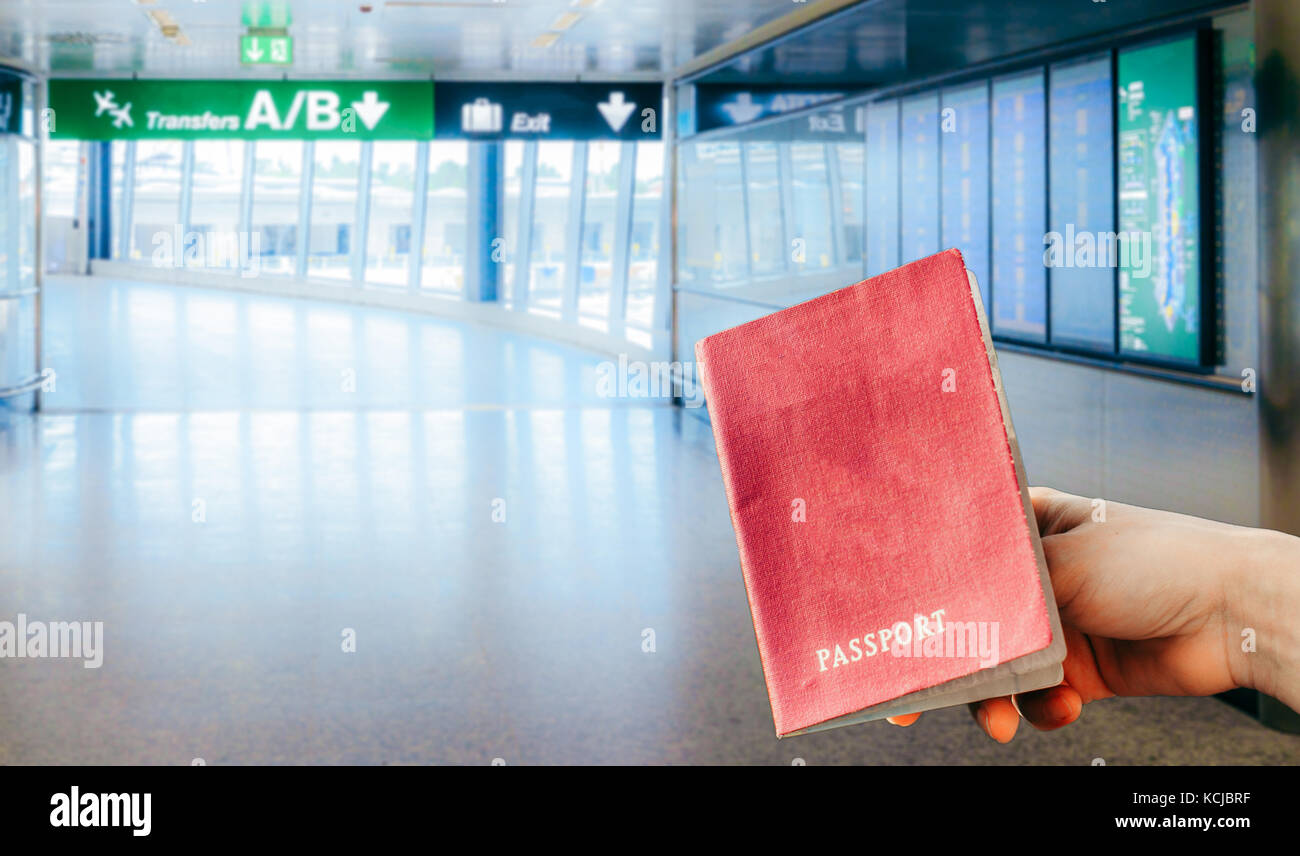 A hand holding an Italian passport at an Italian airport with flight information panels on the right Stock Photo