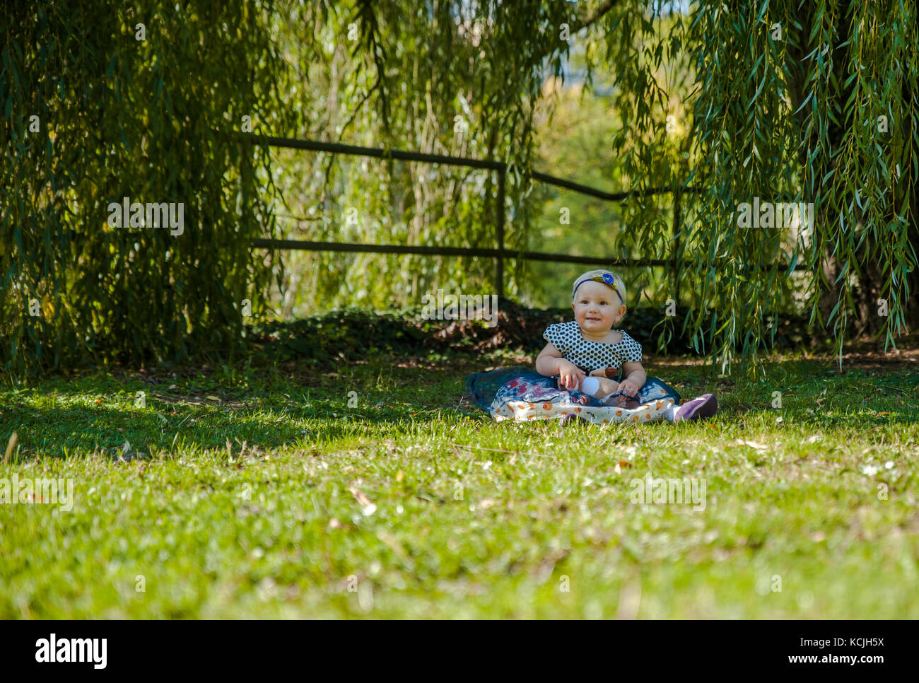 Baby girl sitting on the grass and playing with her teddy bear Stock Photo