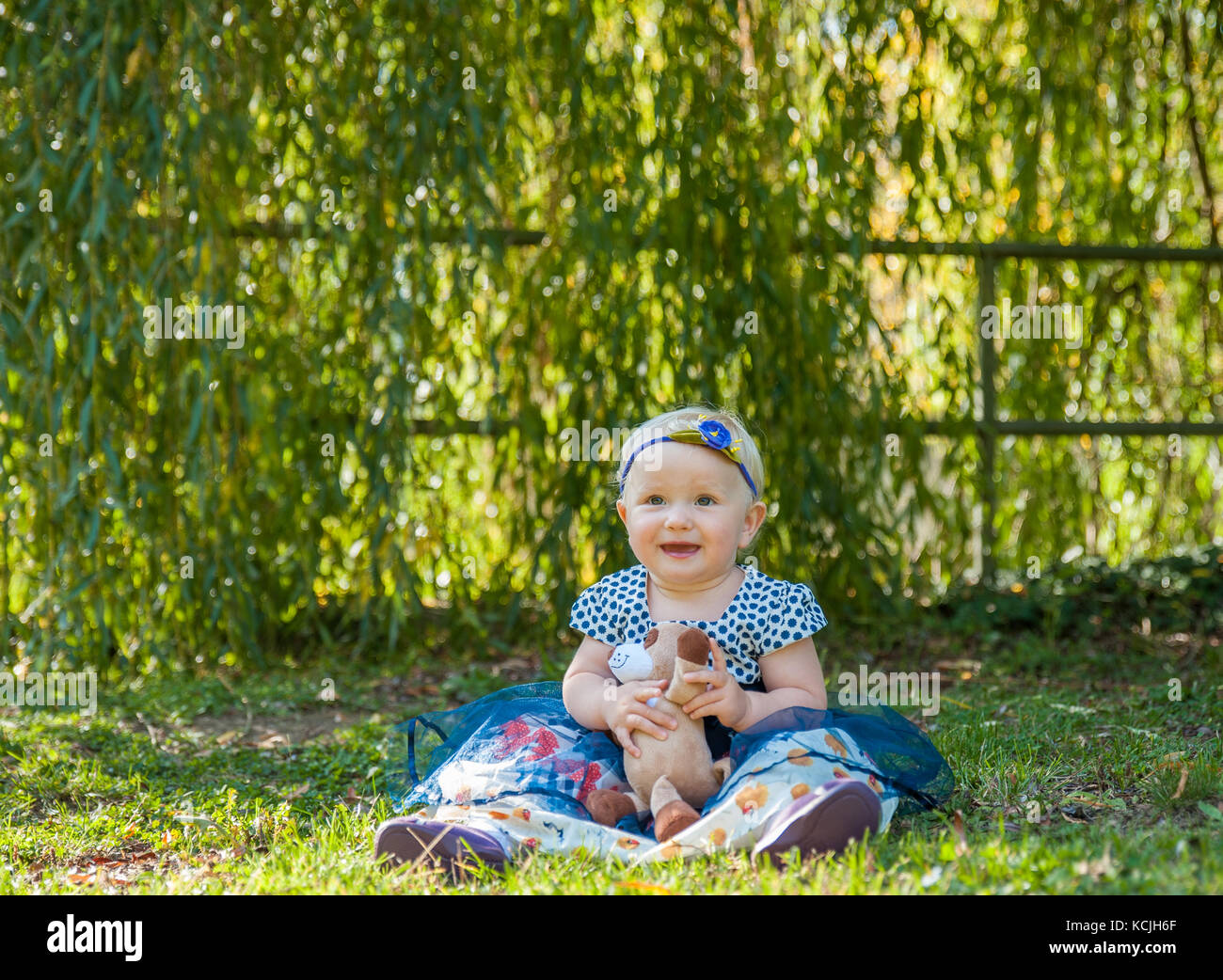 Baby girl sitting on the grass and playing with her teddy bear Stock ...