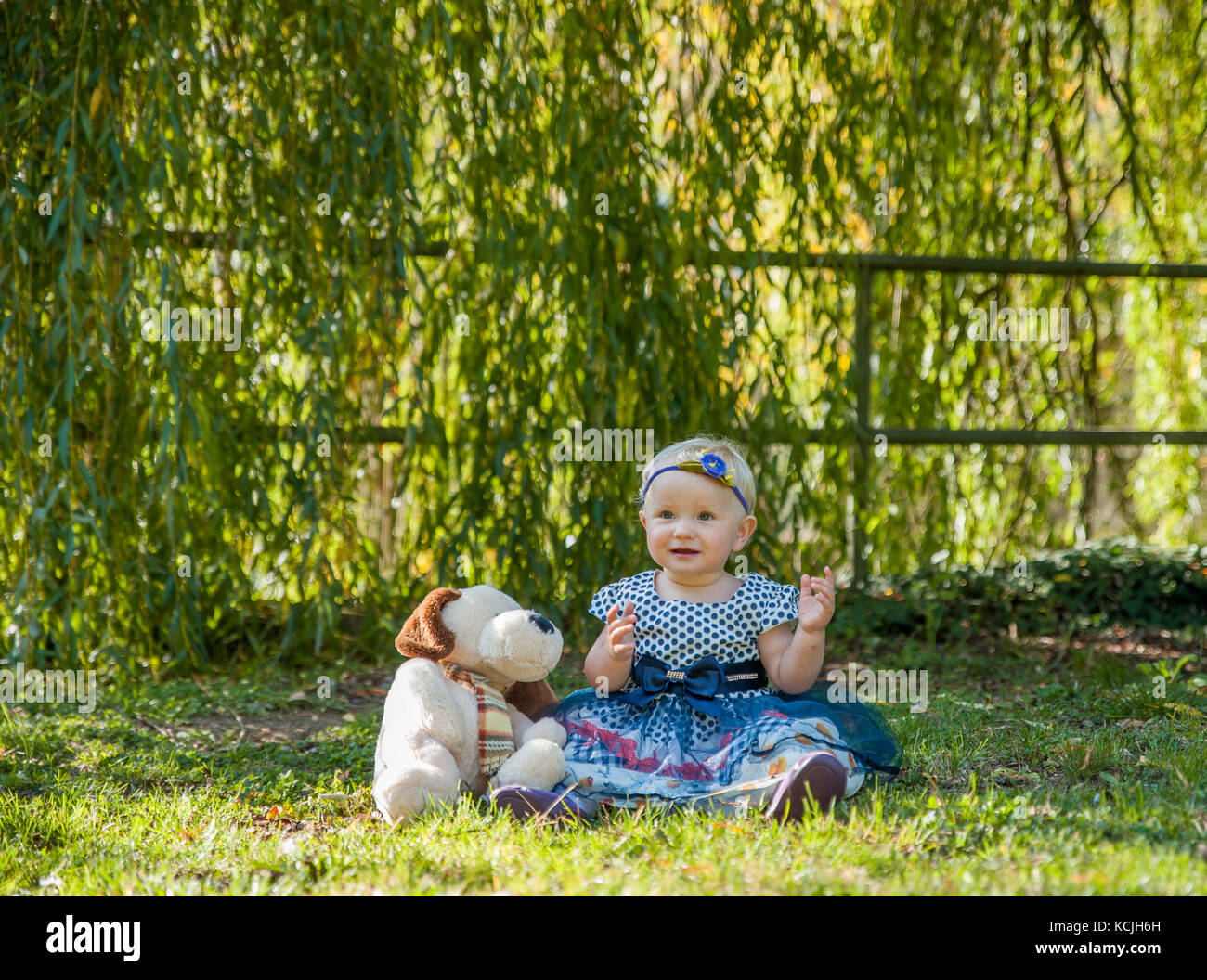 Baby girl sitting on the grass and playing with her teddy bear Stock Photo