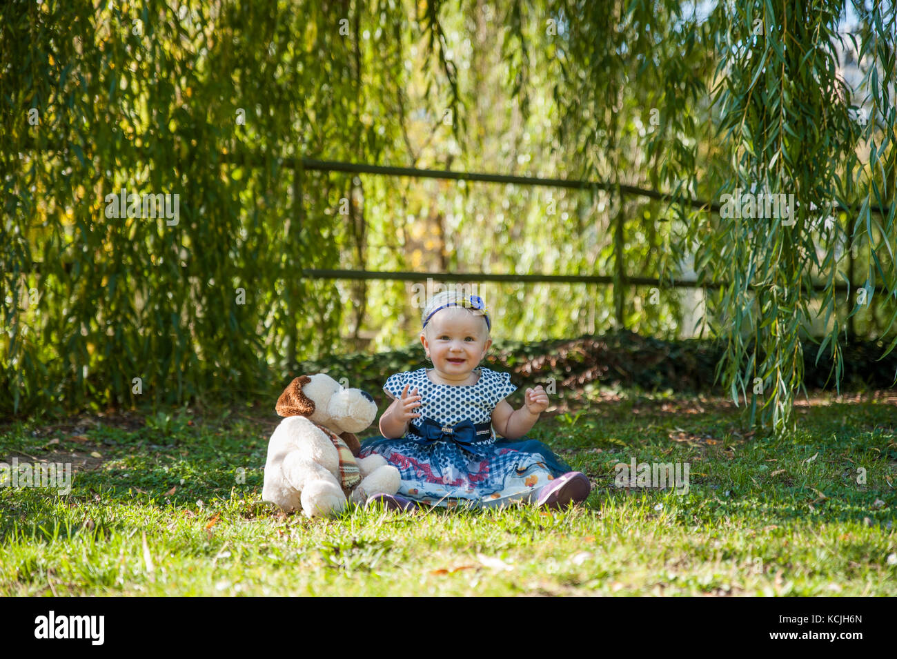 Baby girl sitting on the grass and playing with her teddy bear Stock ...