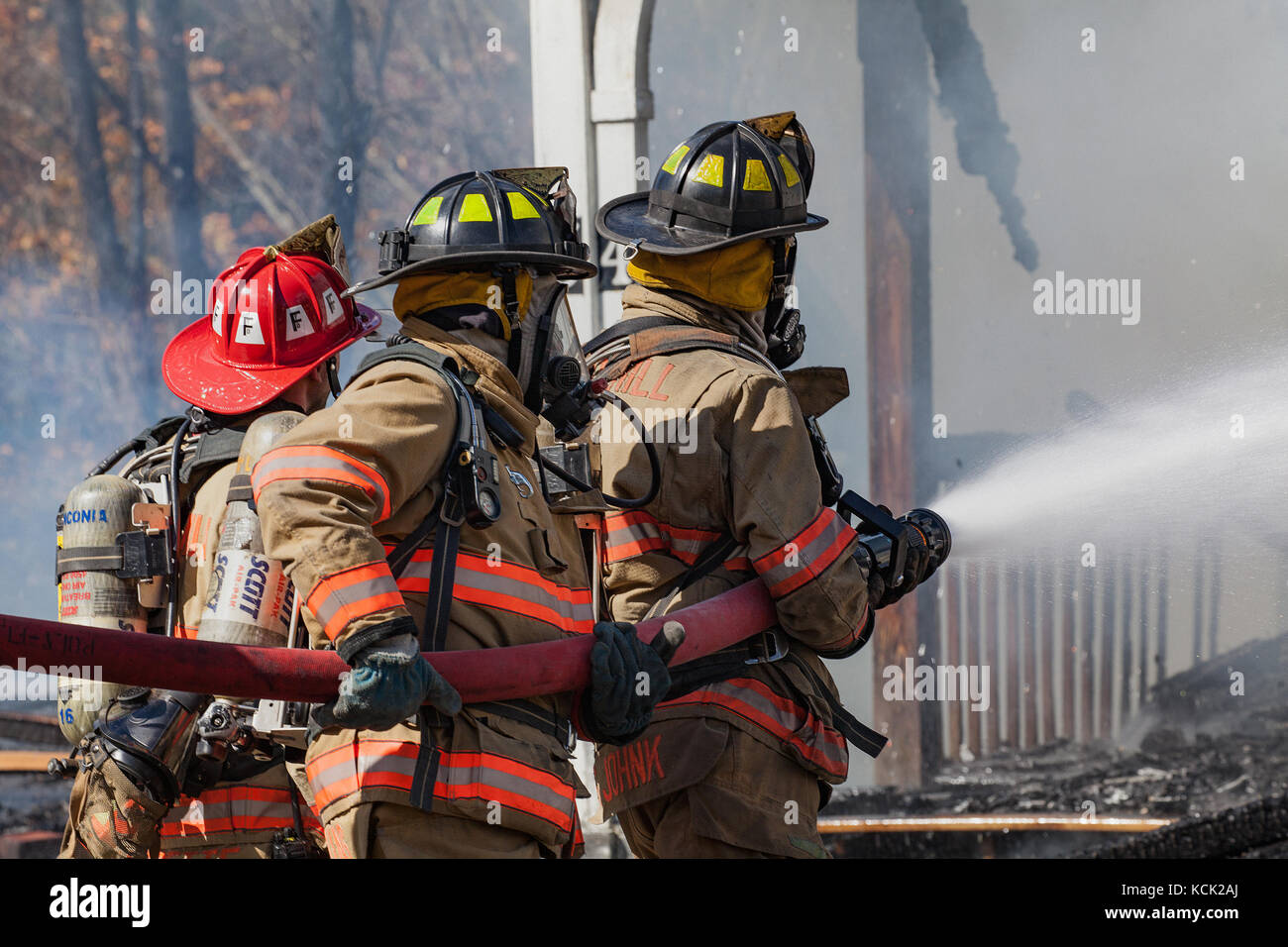 Firemen wearing their full structural firefighting kits battle flames of unknown origin at a house fire in Lisbon, NH, USA on Oct 5, 2017. Stock Photo