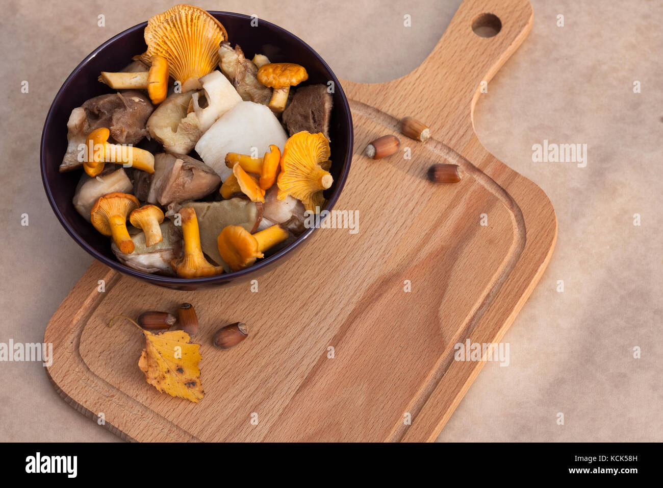 Raw Food. Bowl With Raw Cut Edible Mushrooms (Chanterelle, Cep) And Cutting Wooden Board On Beige Brown Background Top View. Stock Photo