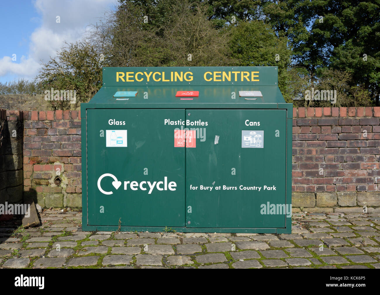 Green painted recycling centre, green steel cabinet holding recycling bins in front of red brick wall, Burrs country park Bury lancashire uk Stock Photo
