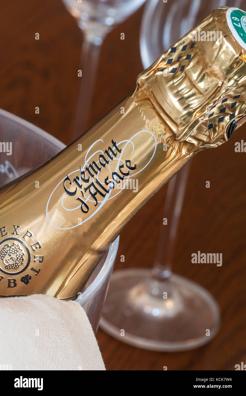 Cremant d’Alsace sparkling wine bottle in ice bucket with glasses behind on dining table Stock Photo