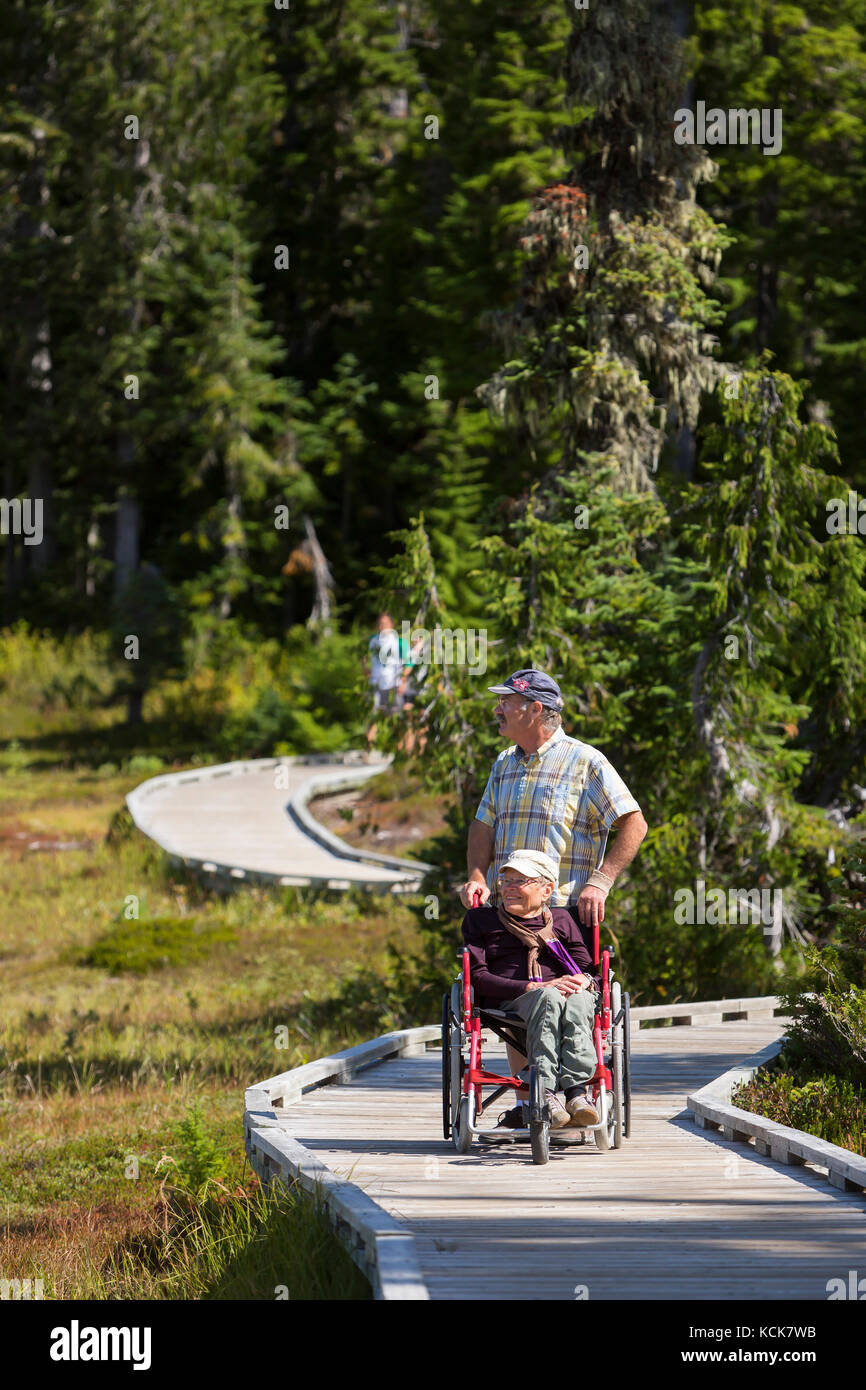 A physically handicapped woman and her partner negotiate a  boardwalk while enjoying an outing in Paradise Meadows near Mt. Washington.  Mt. Washington, Courtenay, The Comox Valley, Vancouver Island, British Columbia, Canada. Stock Photo
