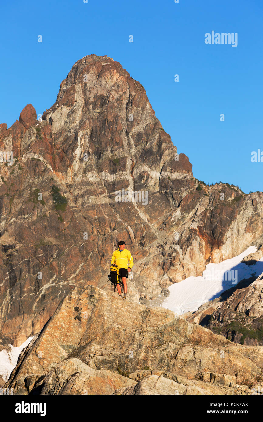 A hiker stands on a rock outcropping with Mt. Septimus in the background, Strathcona Park, Central Vancouver Island, British Columbia, Canada Stock Photo