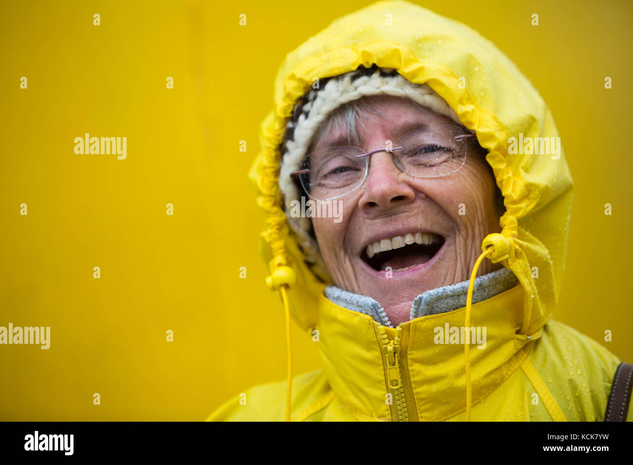 A happy, laughing senior citizen dressed up in her yellow rain slicker enjoys the stormy weather while aboard the MV Uchuck III, Friendly Cove, Vancouver Island, British Columbia, Canada. Stock Photo