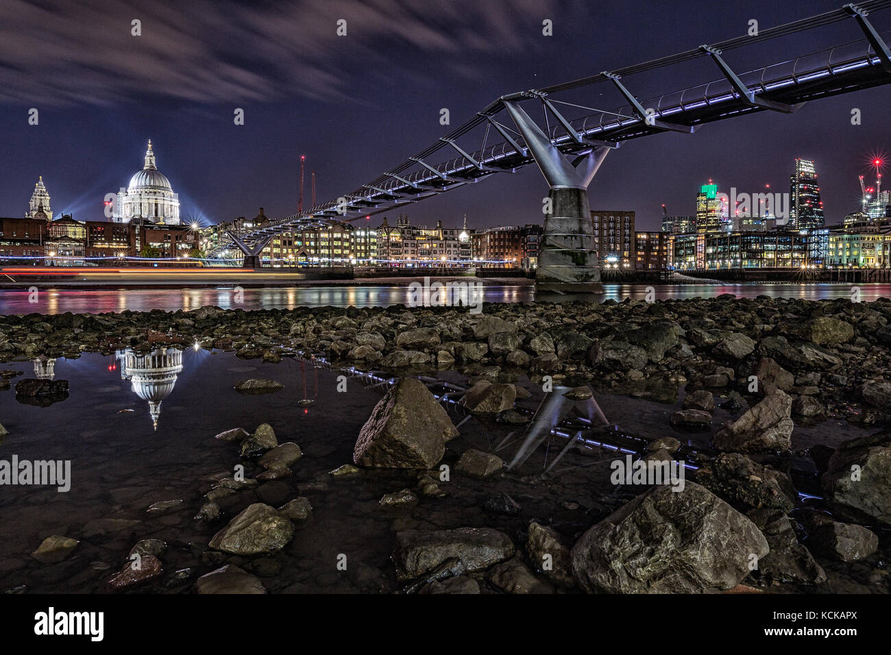 London skyline, Thames bank below St Paul's at low tide, wets rocks and reflections, the Millennium Bridge at night Stock Photo