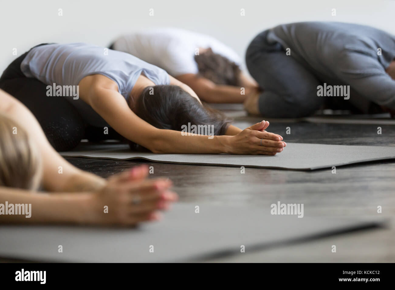 Group of young sporty people practicing yoga lesson with instructor, sitting in Balasana exercise, Child pose, friends working out in club, indoor clo Stock Photo
