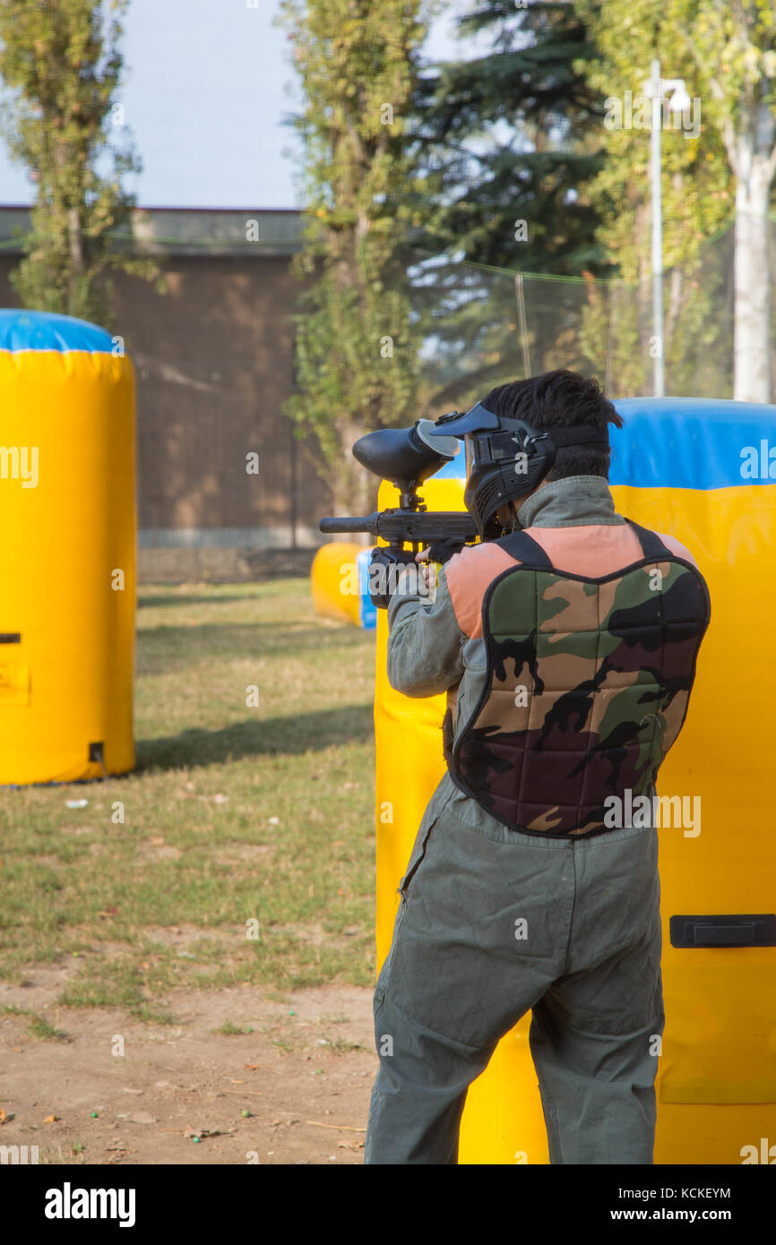Boys Playing Paintball Military Game with Gun, Uniform and Protective Mask behind Yellow Inflatable Stock Photo