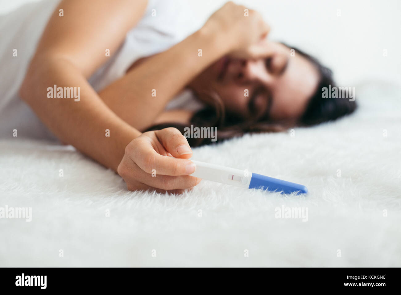 Upset woman lie sad in the bed with negative pregnancy test Stock Photo