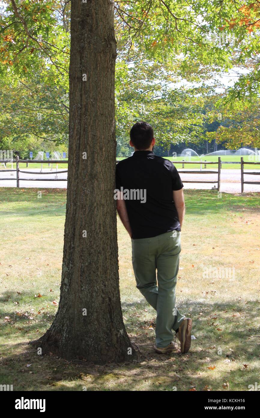 A male model thinking and leaning against a tree in the New England region of the North Atlantic part of Massachusetts Stock Photo