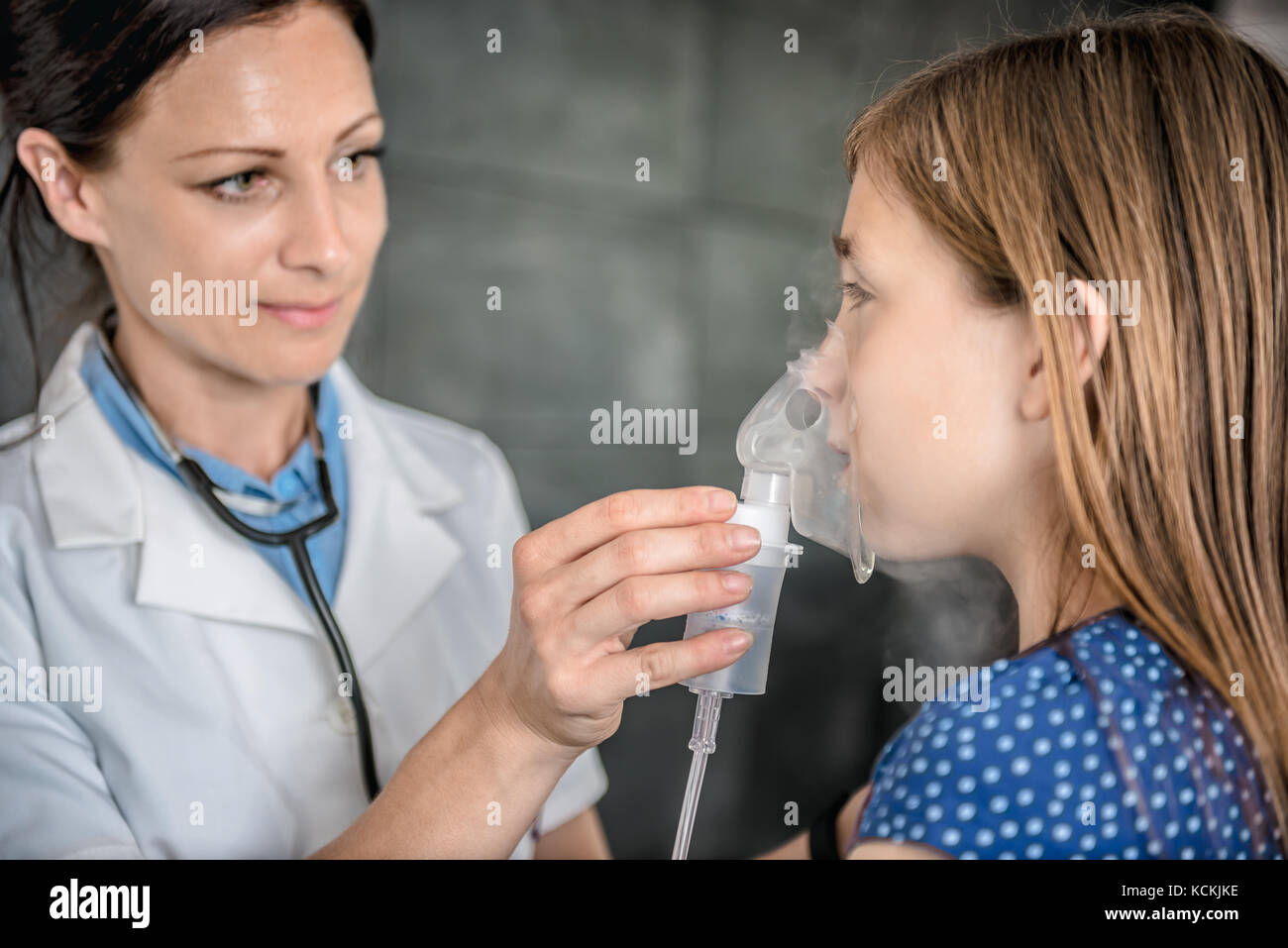 Pediatrics doctor hold a mask vapor inhaler to a little girl breathing through a steam nebulizer Stock Photo