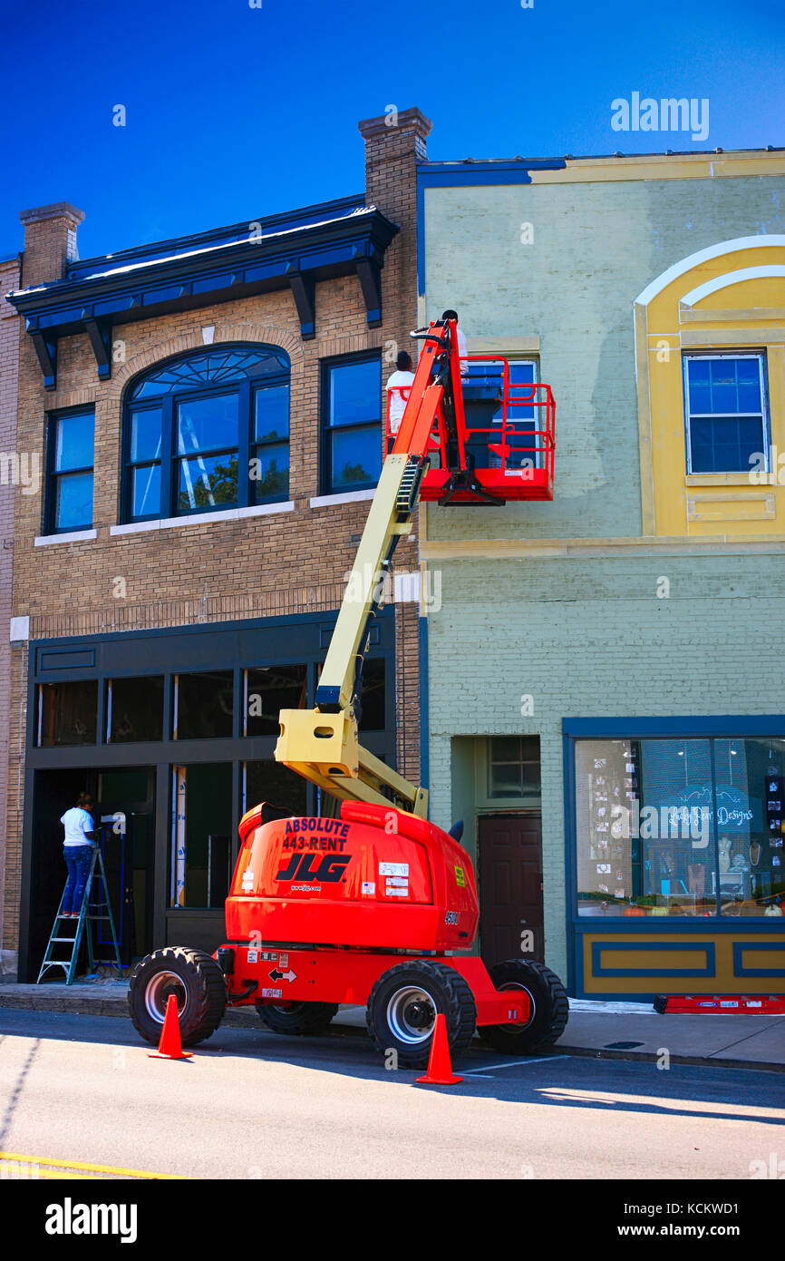 Men using a cherry picker to paint the exterior of a store in downtown