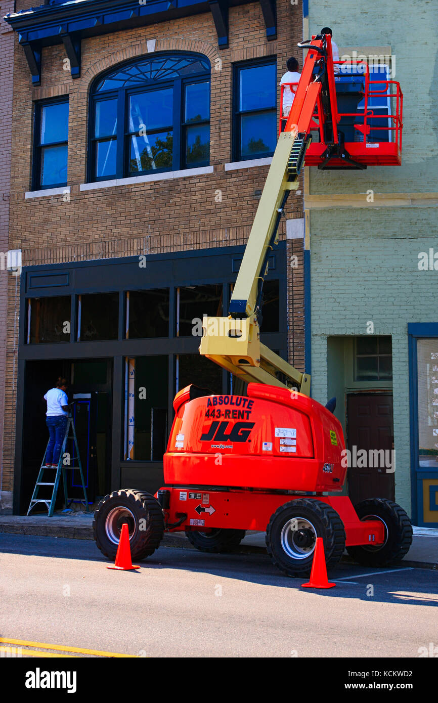 Men using a cherry picker to paint the exterior of a store in downtown