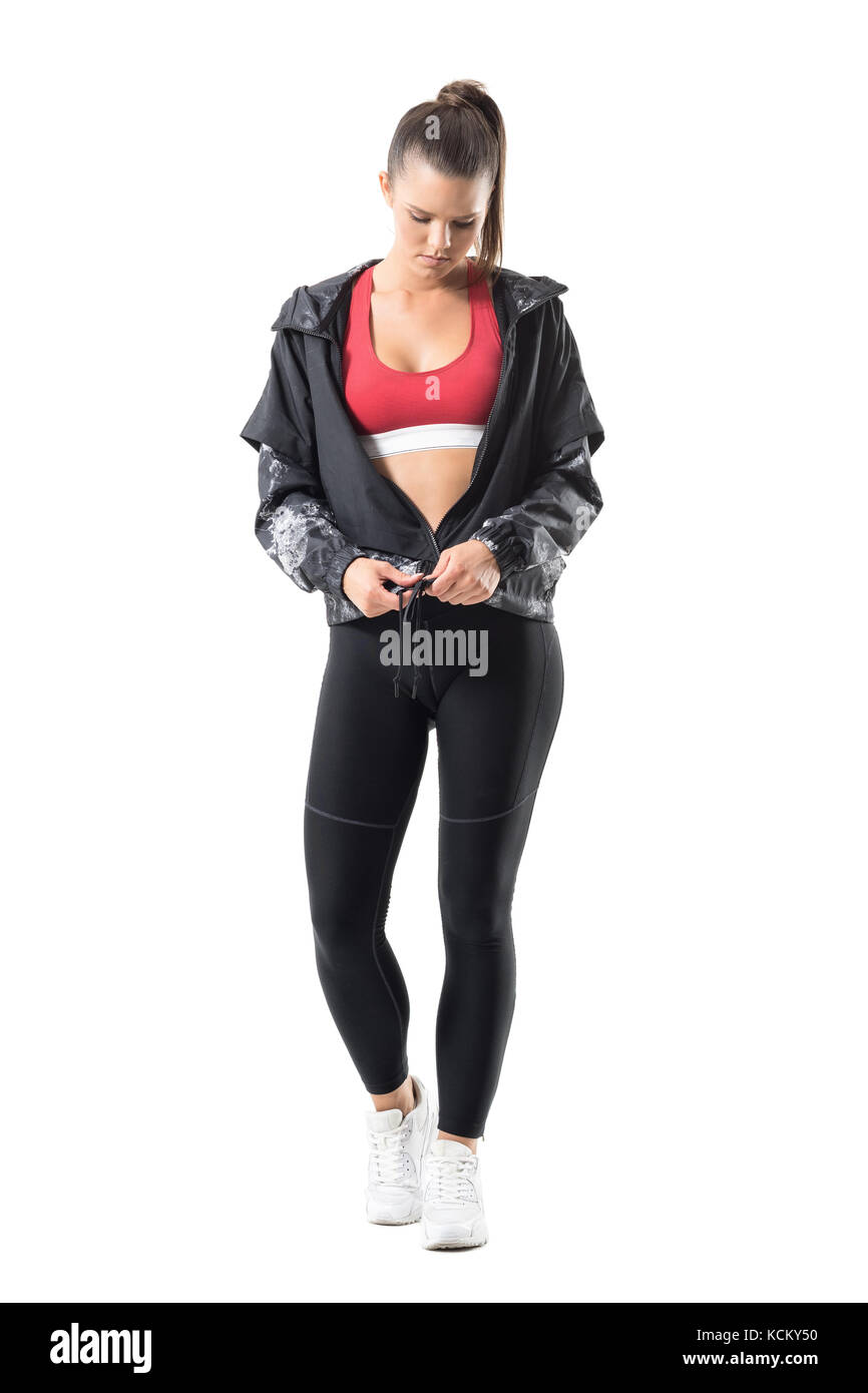 Confident young pretty fit runner in sportswear zipping tracksuit jacket get dressed. Full body length portrait isolated on white background. Stock Photo