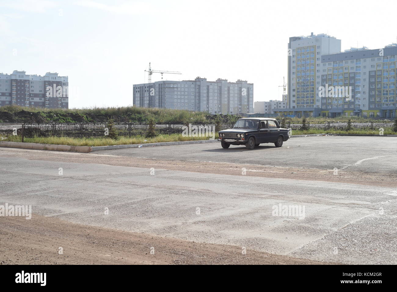 Single old Russian Lada parked in an empty car park with houses and mass apartment blocks in the background Stock Photo