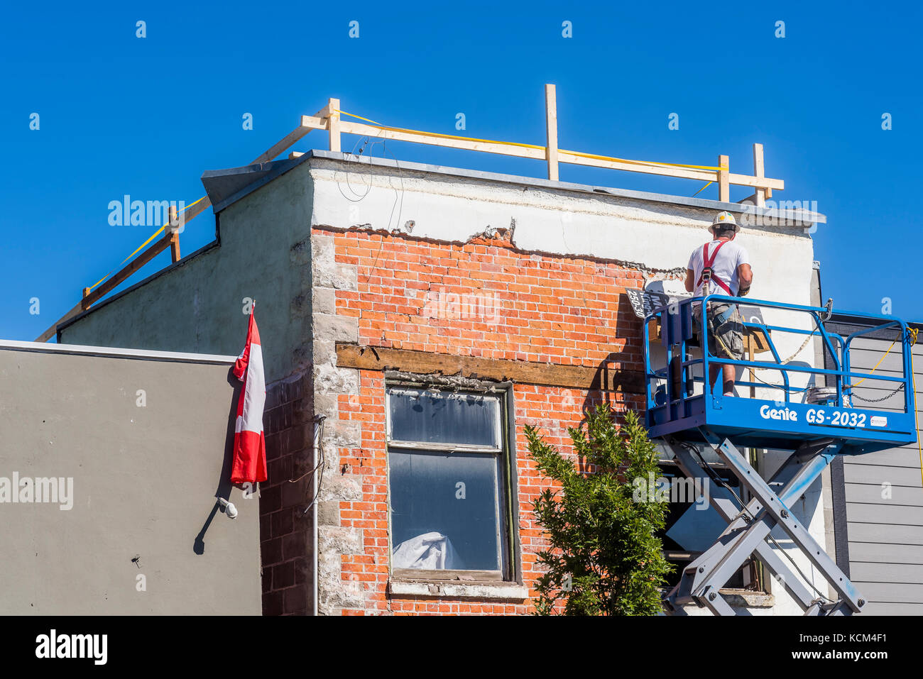 Man removing plaster exterior to reveal original bricks of building, Enderby, British Columbia, Canada. Stock Photo
