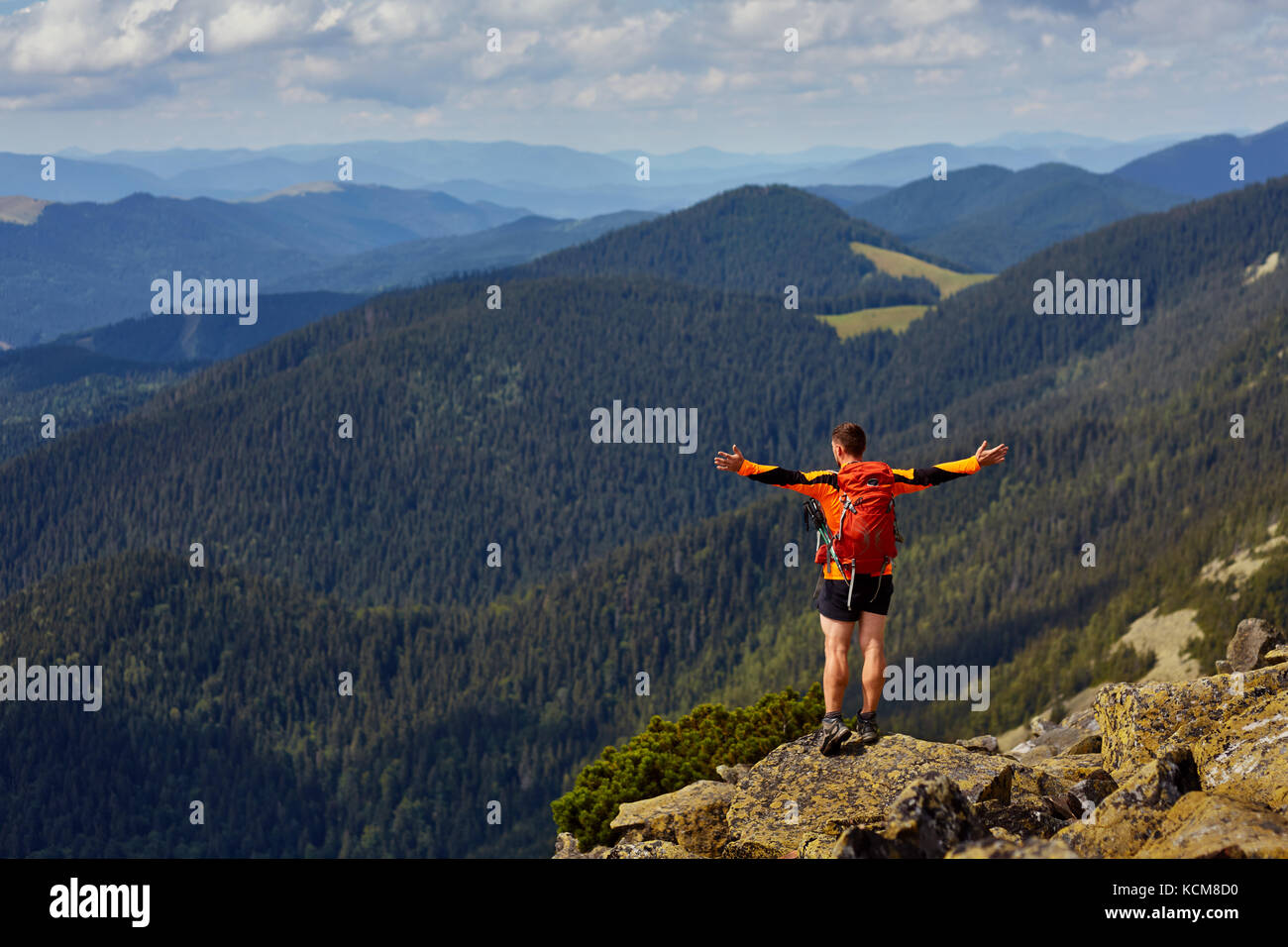 Hiker with backpack standing on top of a mountain with raised hands and ...