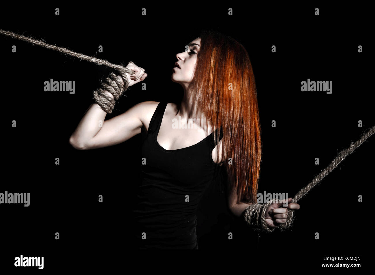 Beautiful young woman with bright red hair and tied arms over black background Stock Photo