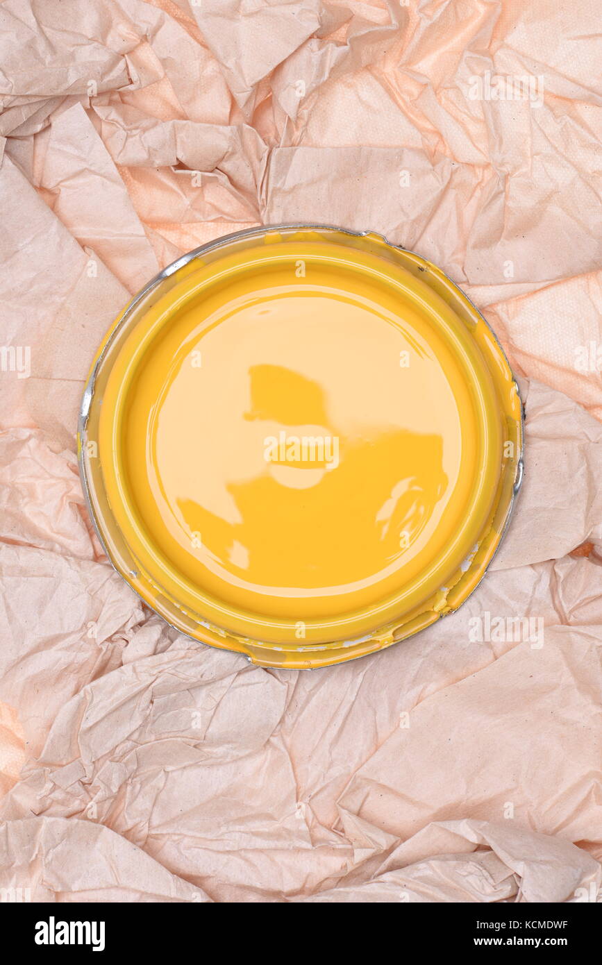 Can lid with yellow paint on crumpled paper, top view Stock Photo