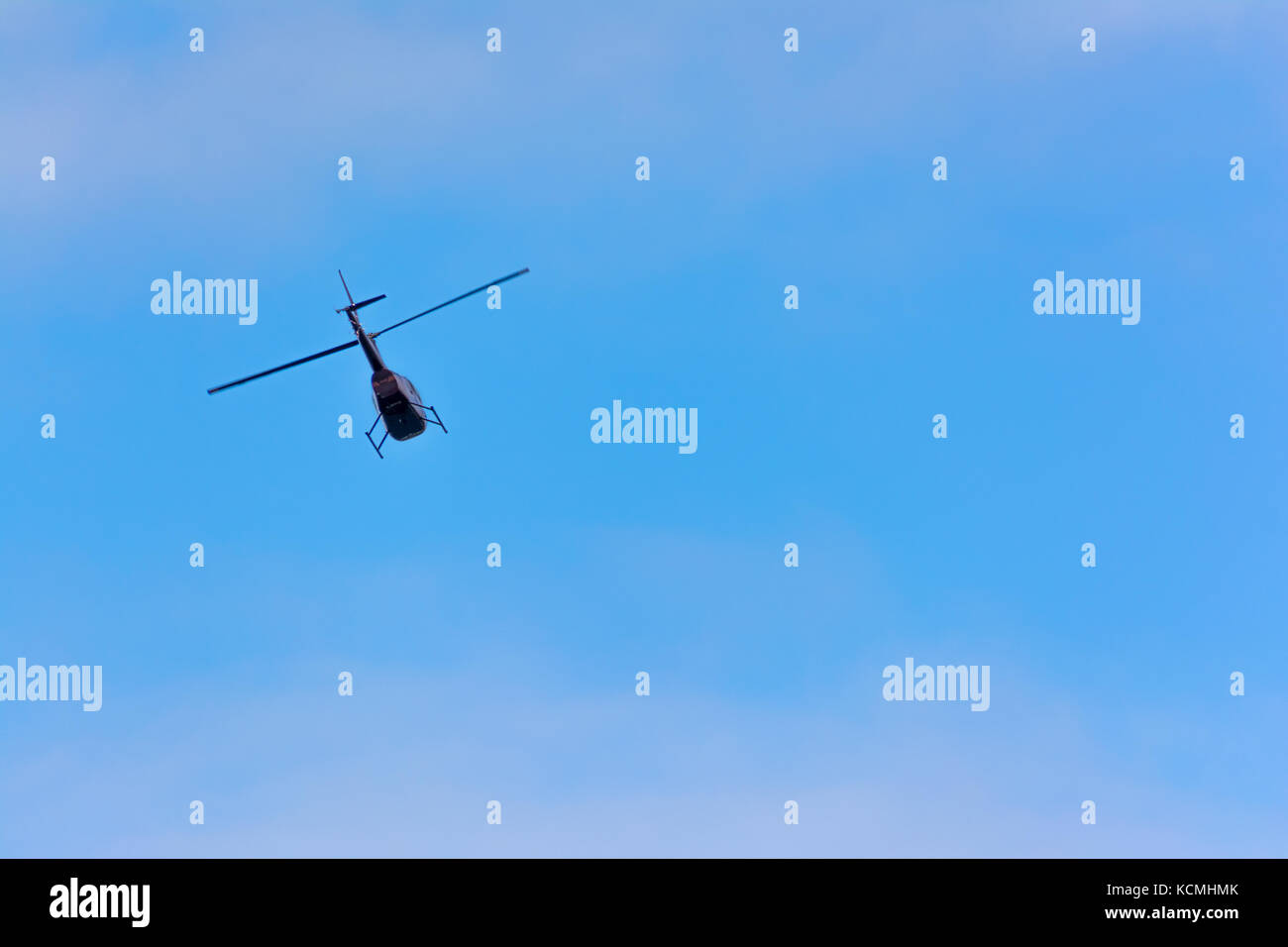 Helicopter flying through blue skies with soft clouds Stock Photo