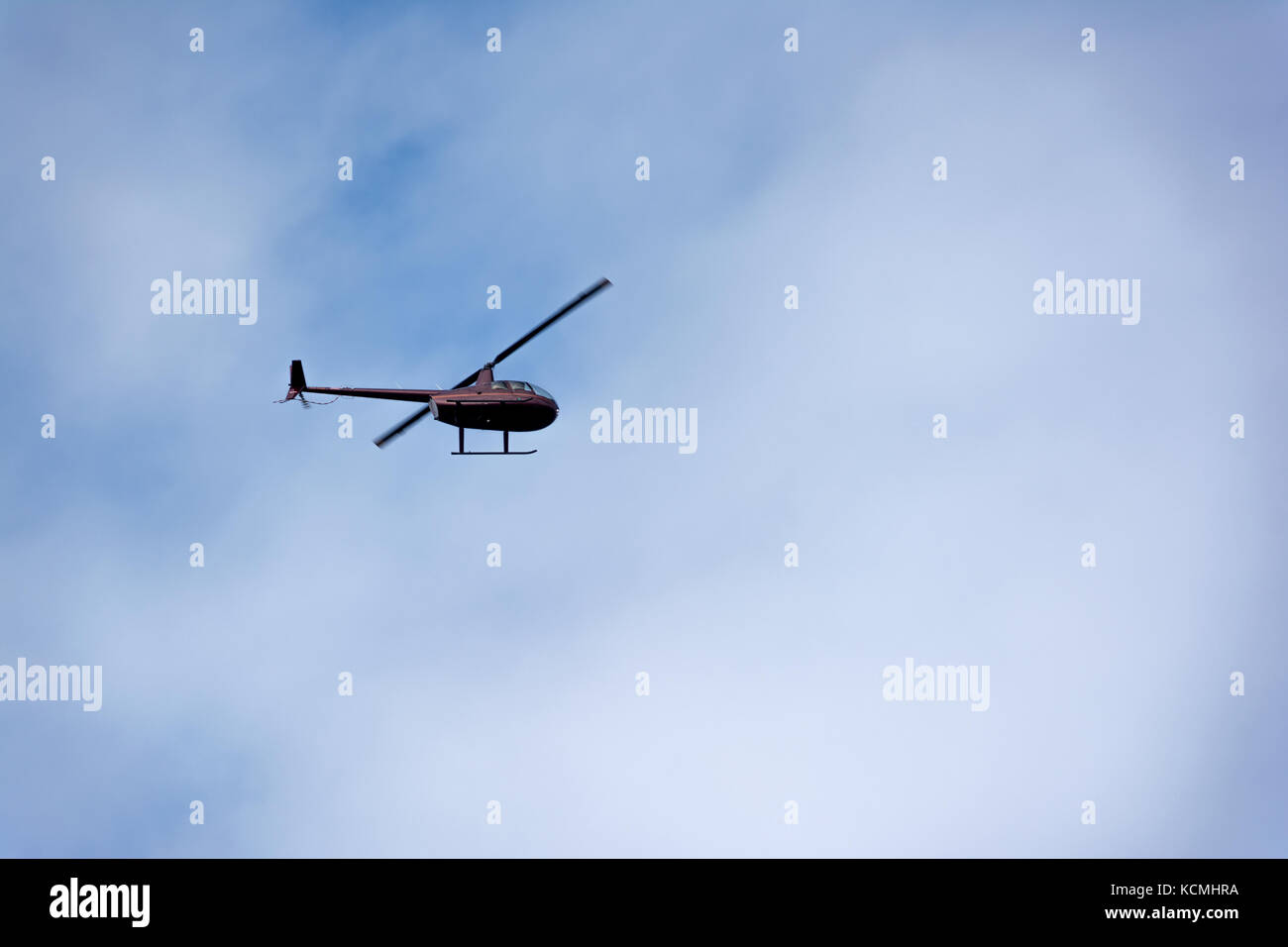 Helicopter flying through blue skies with soft clouds in the background Stock Photo