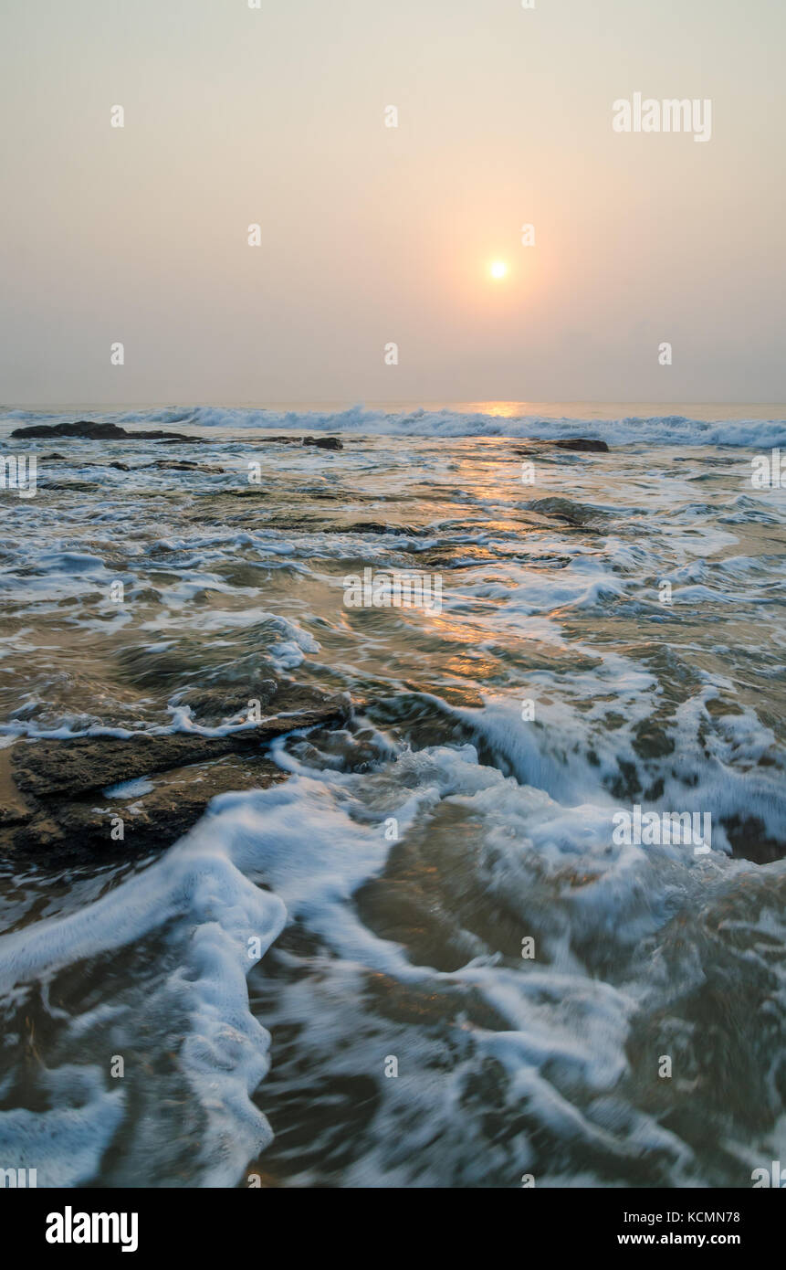 Beautiful sunrise with soft light and wet rocks at beach of Atlantic ocean, Ghana, West Africa Stock Photo