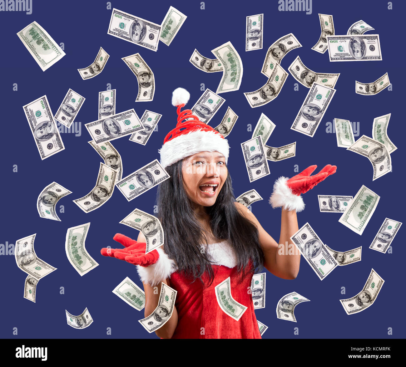 Cheerful Mrs. Claus looks at the camera with her hands showing flying money. Dollar bills are falling around Mrs. Santa Claus. Stock Photo