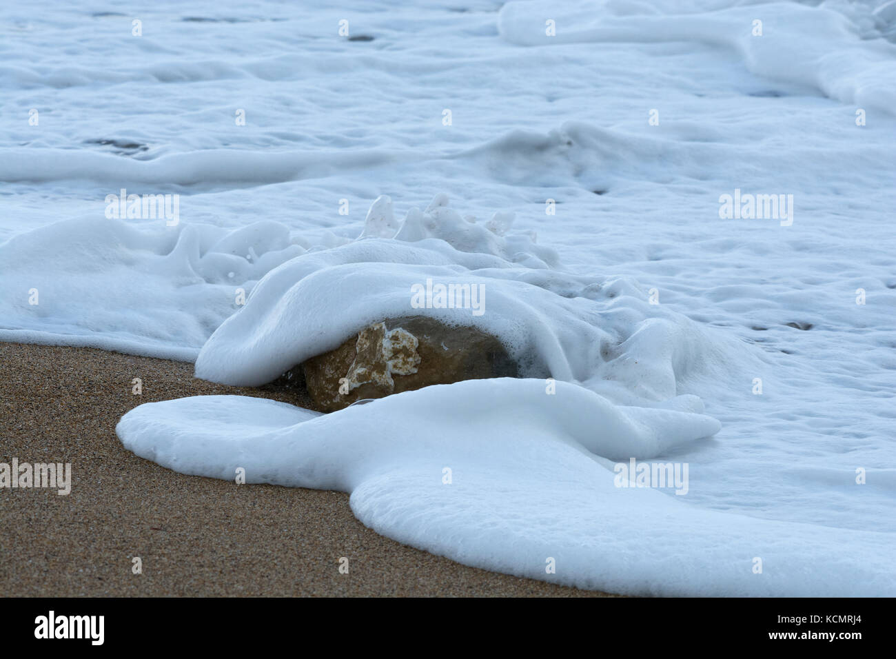 Single stone in surf on sandy beach, West Bay, Dorset, UK Stock Photo