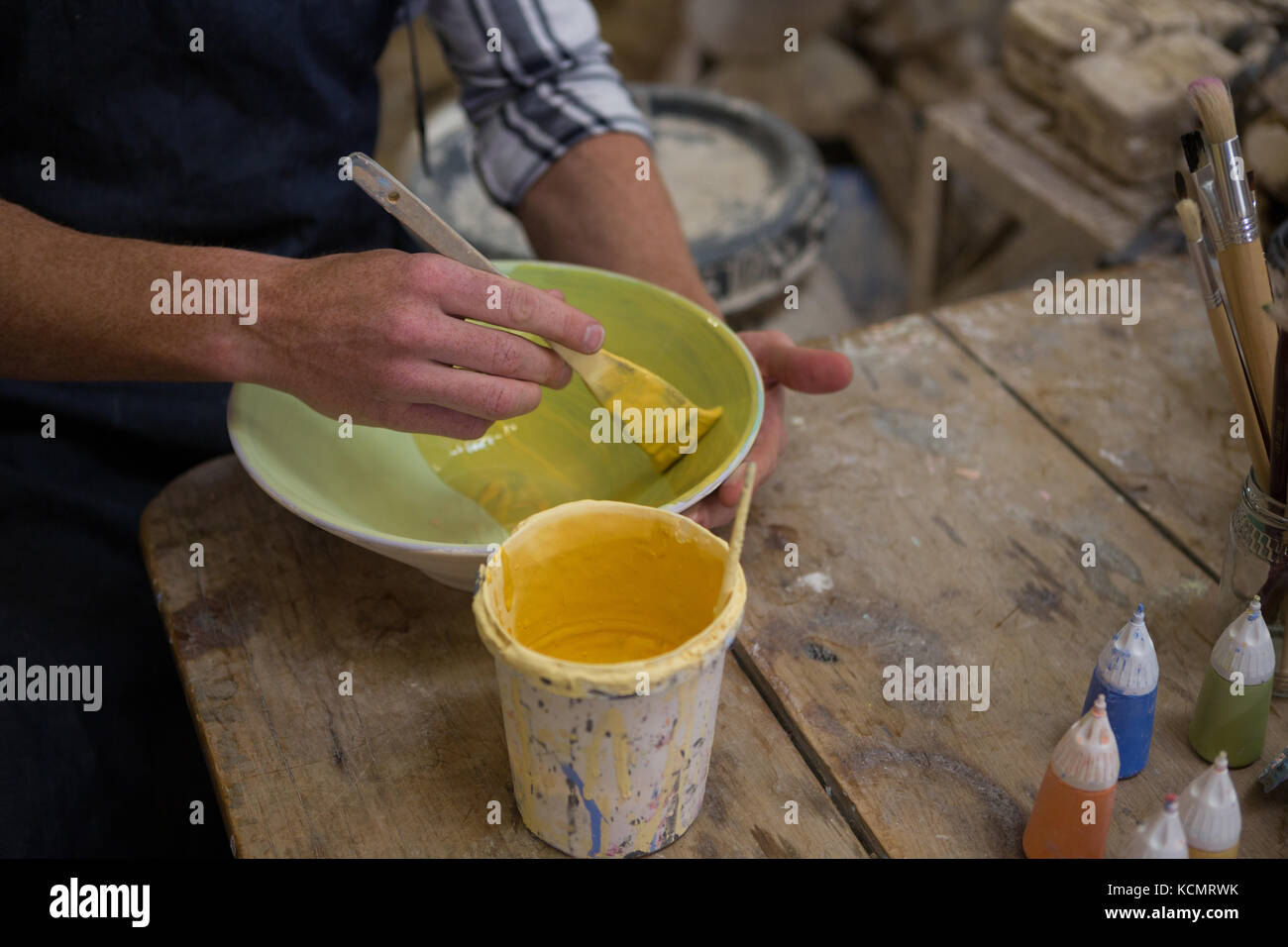 Mid-secion of male potters hand painting a bowl in pottery workshop ...