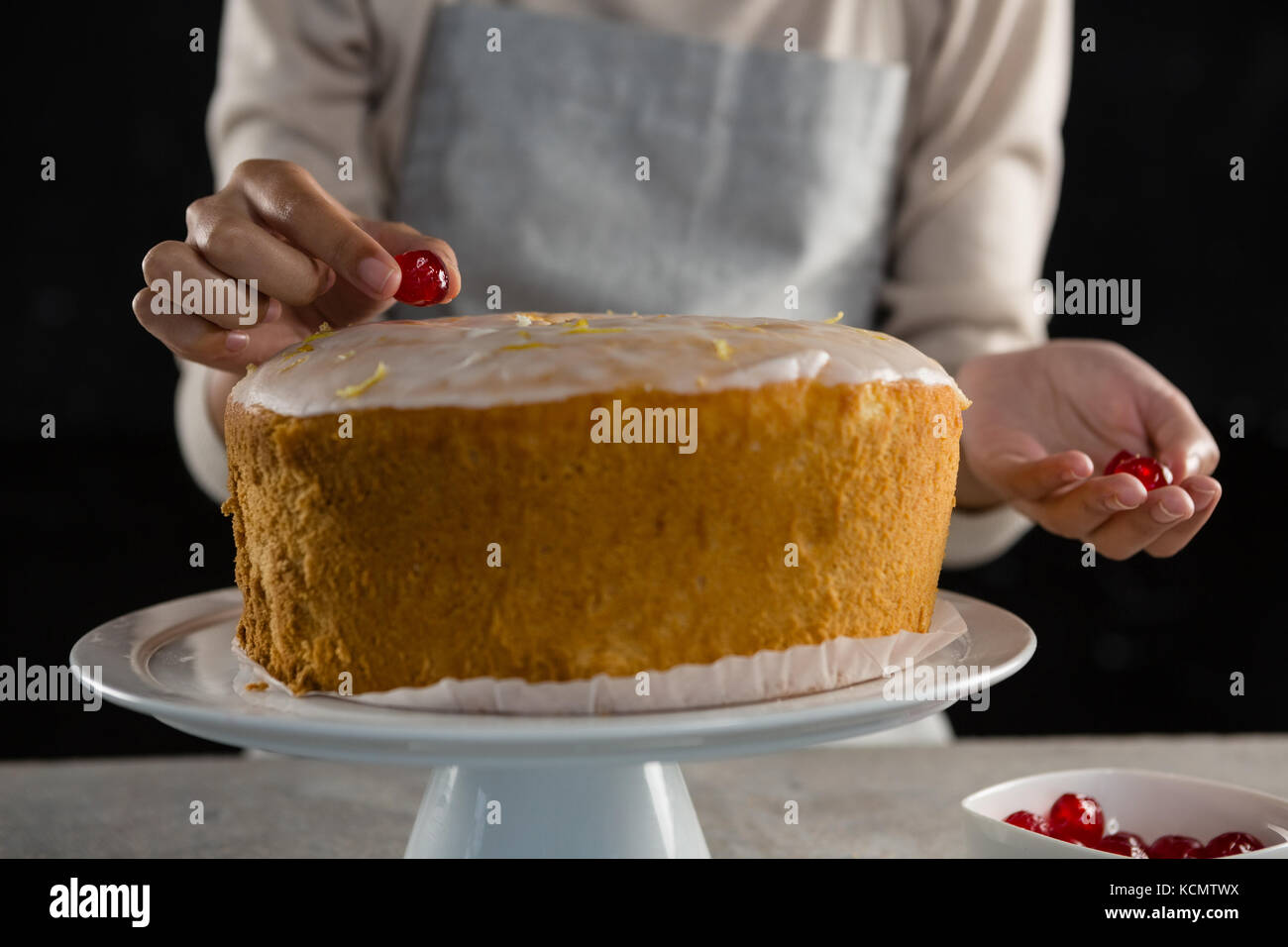 Mid section of woman toping a fresh baked cake with cherry Stock Photo