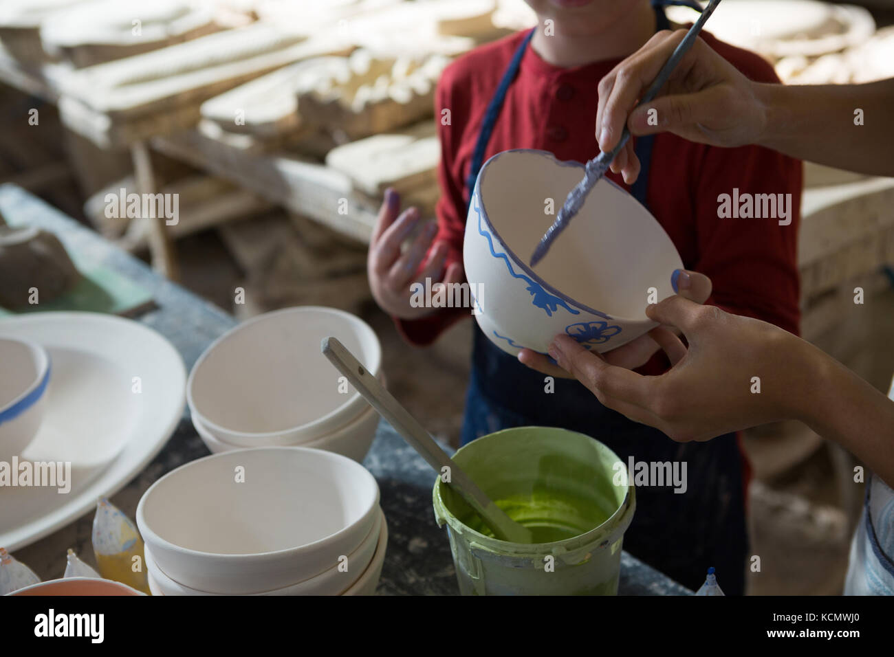 Mid section of female potter and boy painting bowl in pottery workshop ...