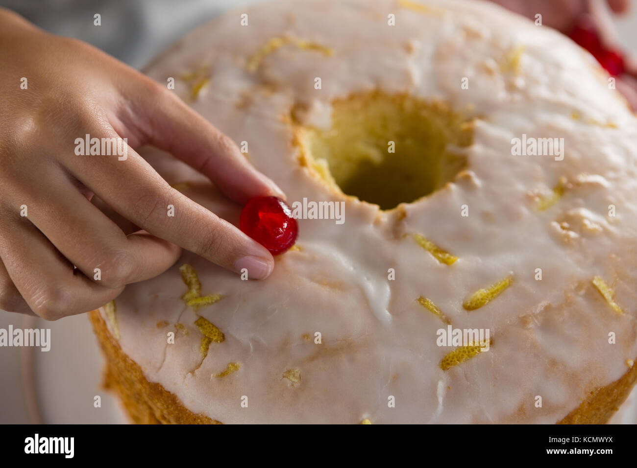 Close-up of woman toping a fresh baked cake with cherry Stock Photo
