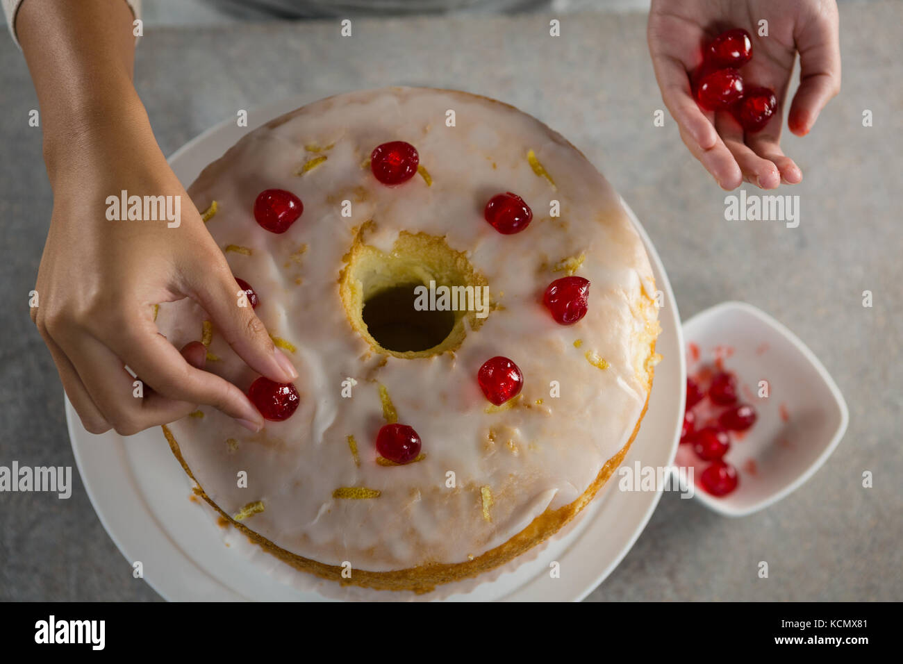 Over head view of woman toping a fresh baked cake with cherry Stock Photo