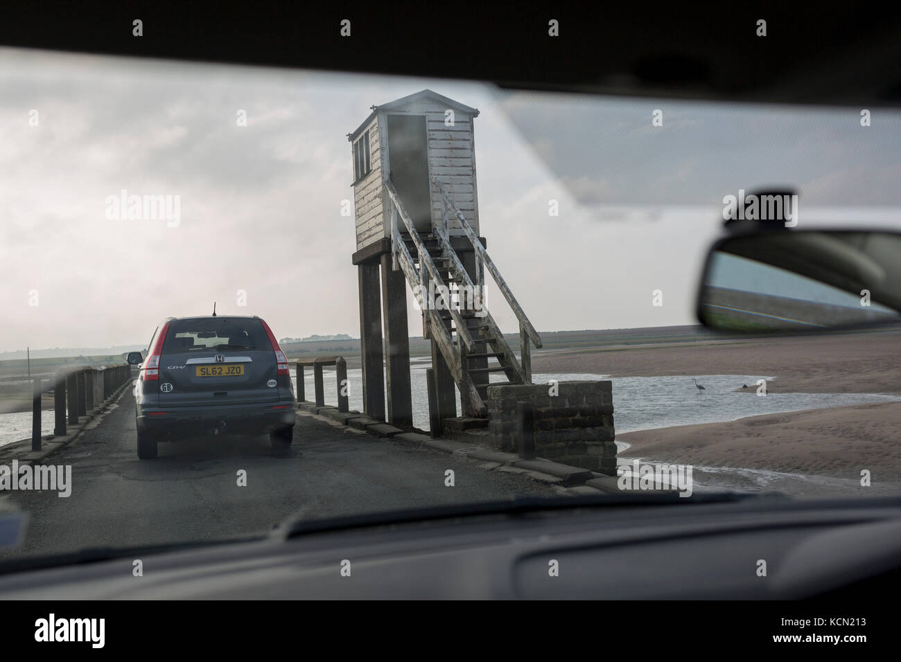 The view through a car's windscreen on the journey over the causeway between the tidal Lindisfarne island and the Northumbrian mainland, on 27th September 2017, on Lindisfarne Island, Northumberland, England. Despite tide timetables posted all over the area, drivers often mis-time their crossings, their vehicles ending up submerged in salt water. The small Lindisfarne population of just over 160 is swelled by the influx of over 650,000 visitors from all over the world every year. A tidal Island: Lindisfarne is a tidal island in that access is by a paved causeway which is covered by the North S Stock Photo