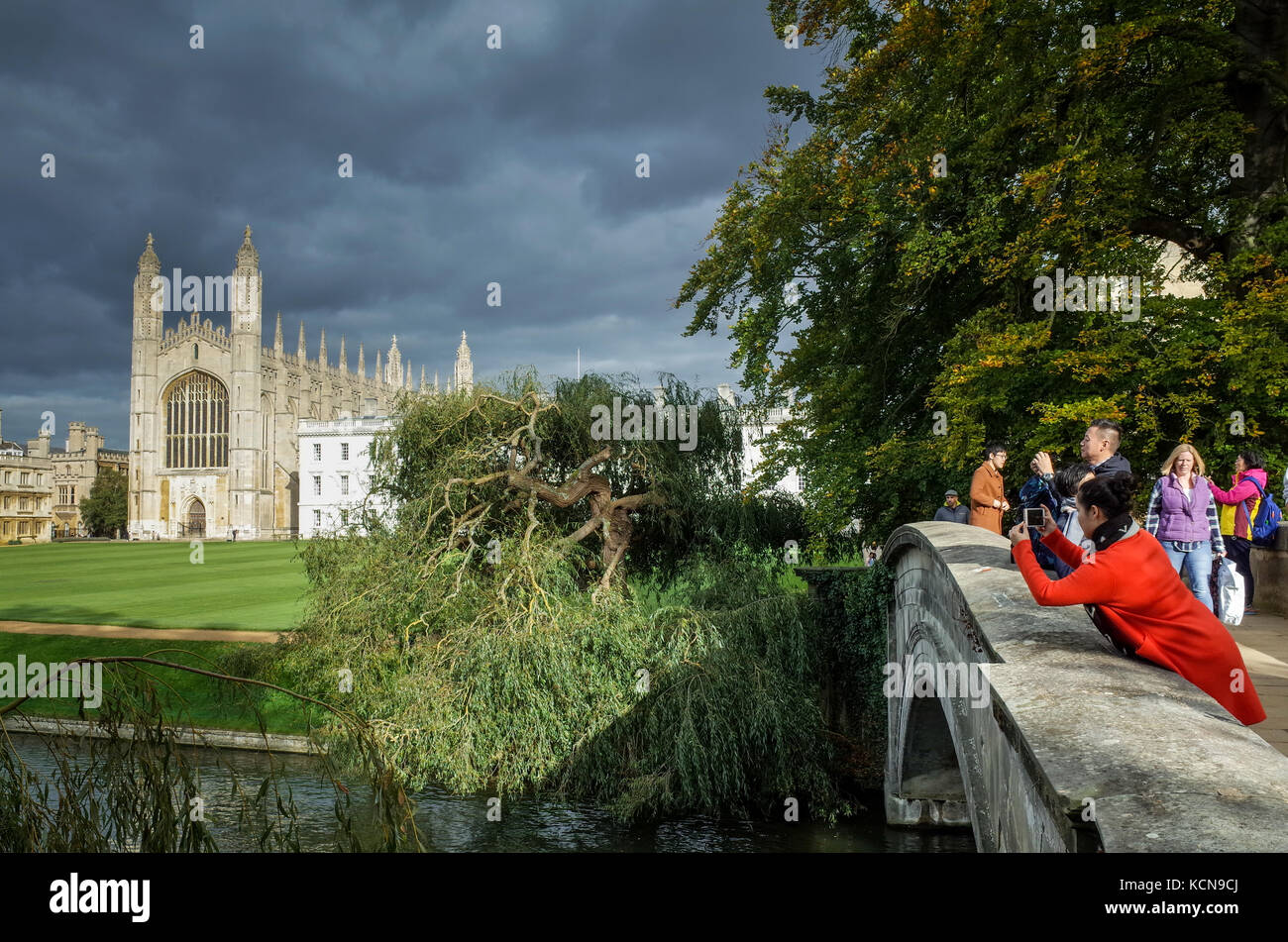 Cambridge Tourism - Cambridge tourists take photos of the famous Kings College Chapel, lit by evening sunlight under dark skies. Stock Photo