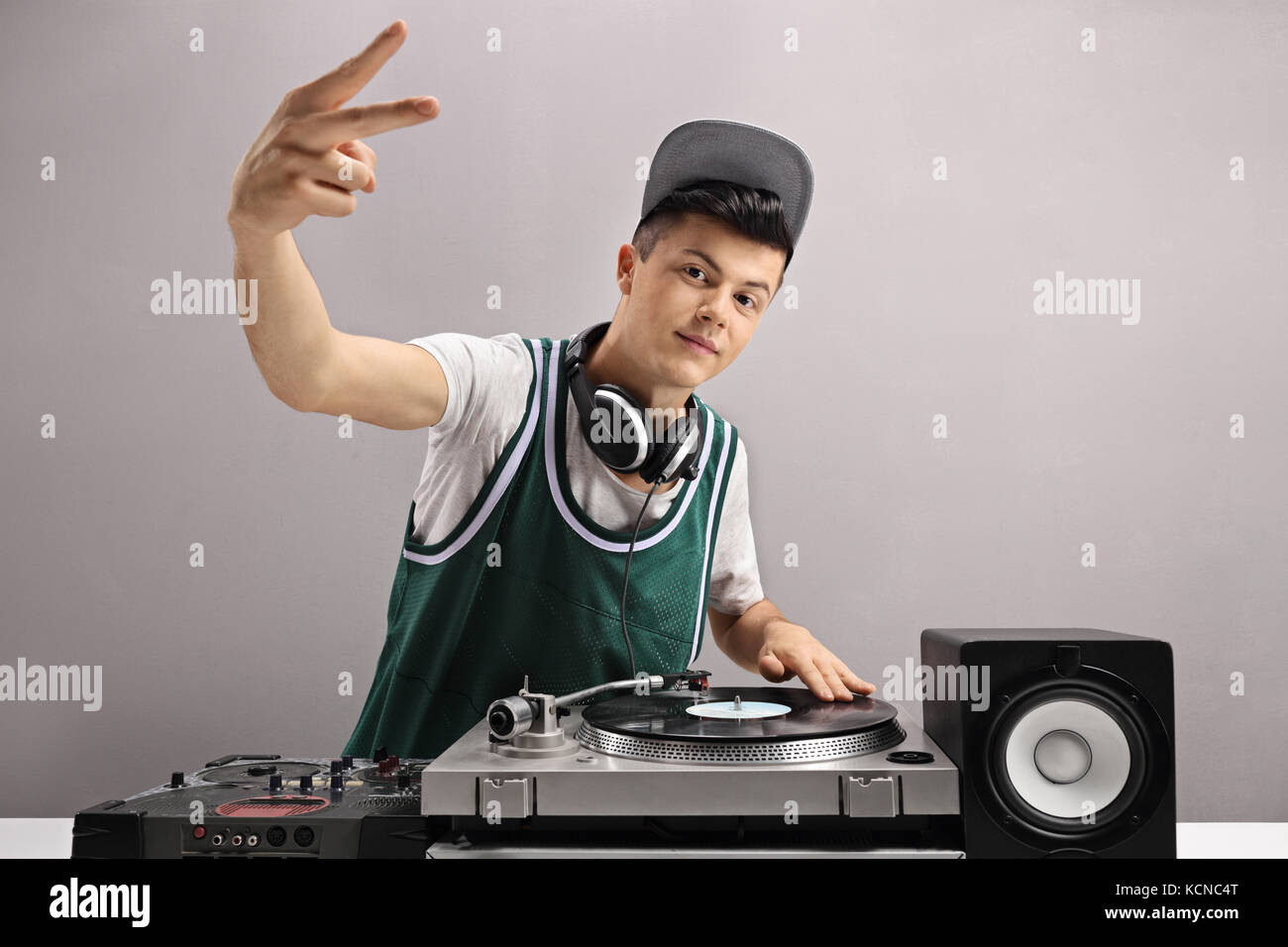 Teenage DJ making a peace sign against a gray wall Stock Photo