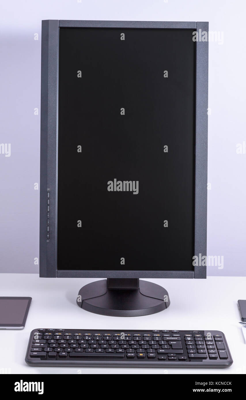 Black blank pc monitor turned vertical and keyboard on desk. Stock Photo