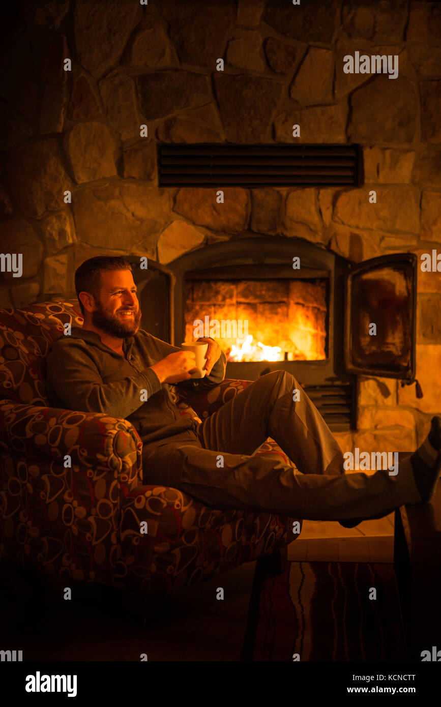 Man (40) sitting by a warm open fire at a log cabin ski chalet in Mont Tremblant, Quebec, Canada Stock Photo