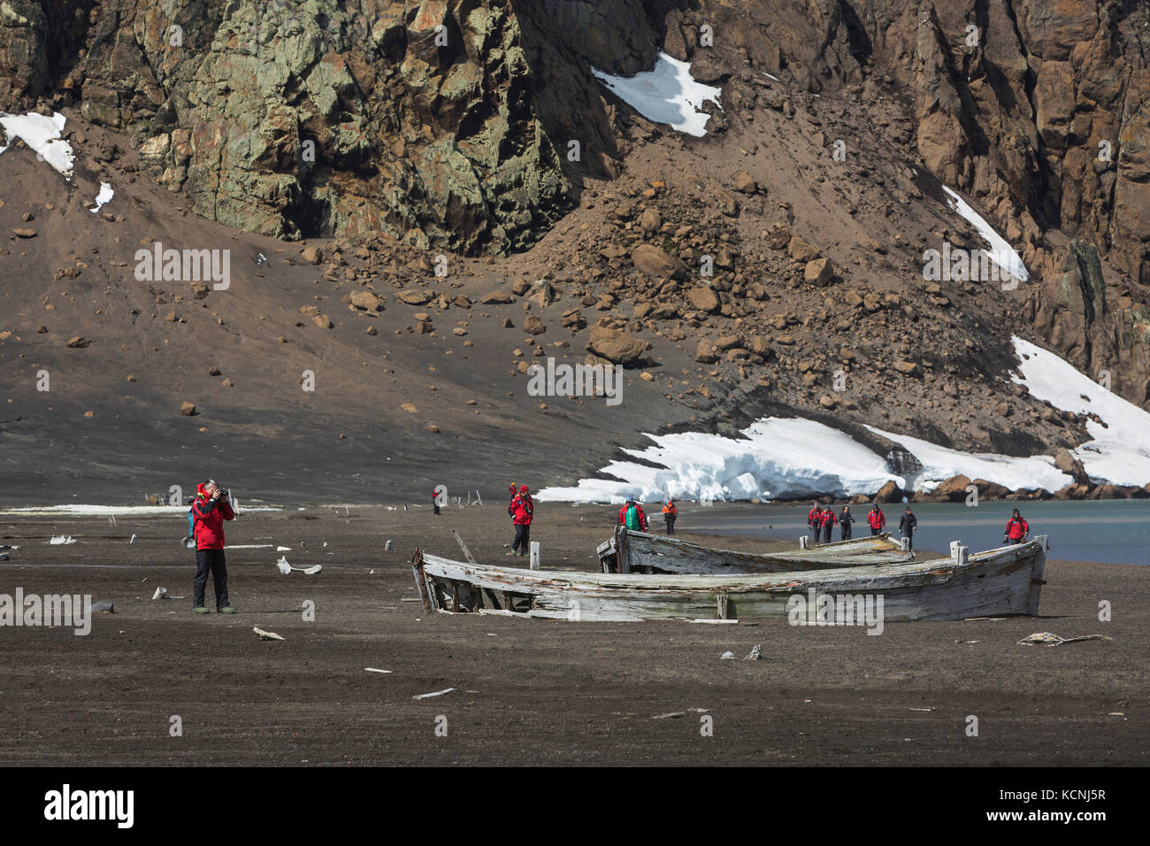 Adventure tourists walk near long abandoned water boats from the whaling era on a volcanic beach at Whalers Bay, Deception Island, South Shetland Islands Stock Photo