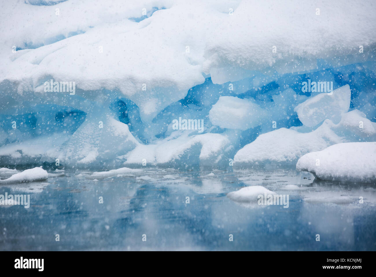 Snow falling on a grounded iceberg near Pleneau Island with its many hues of blue gives the impression of being inside a snowglobe, Pleneau Island, Antarctic  Peninsula Stock Photo