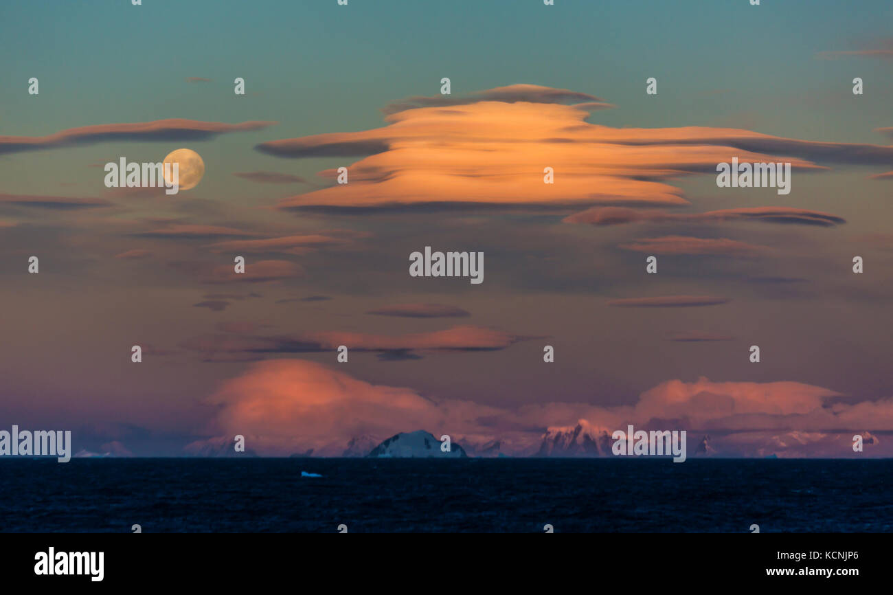 Dramatic Lenticular clouds share an evening sky with a full moon overlooking the Gerlache Strait, Antarctic Peninsula Stock Photo