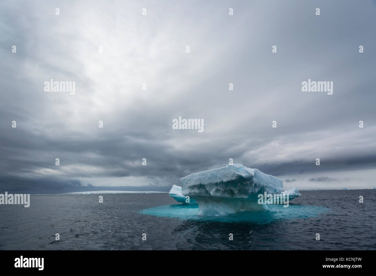 An iceberg undercut by water remains floating with its undwerwater foot against a dramatic sky.  Joinville Island, Antarctic Peninsula. Stock Photo