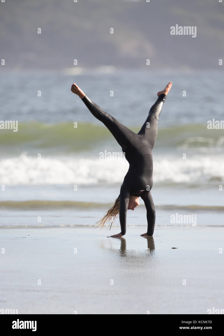 A female surfer shows off her gymnastic skills while on Chesterman Beach, Tofino, Vancouver Island, British Columbia, Canada Stock Photo